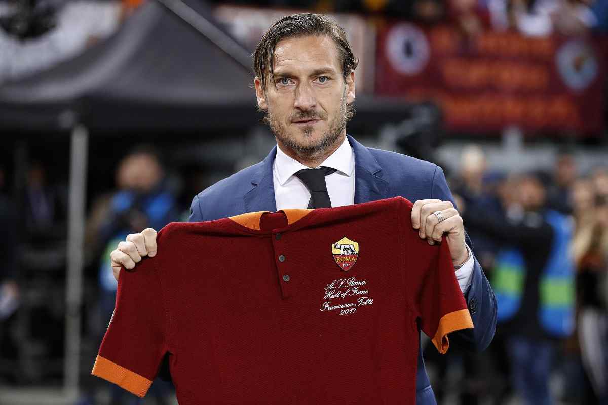 Francesco Totti in giacca e cravatta che mostra una maglia della Roma